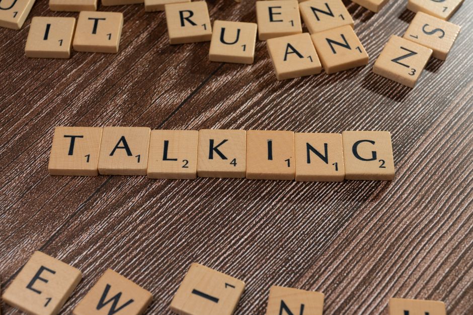 Imagem com peças de jogo de palavras formando a frase 'Talking', simbolizando comunicação e expressão verbal.