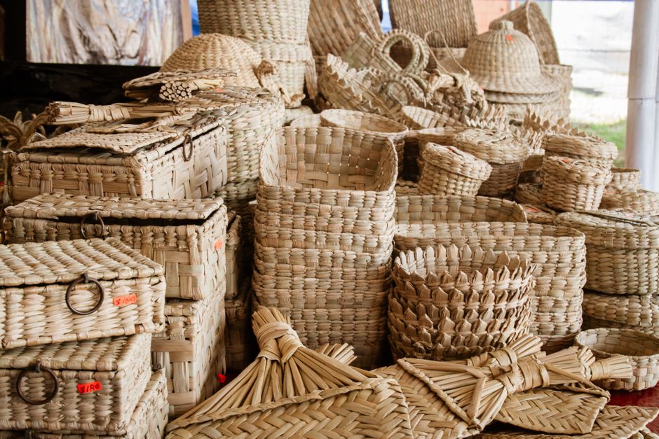 Vaso de vasos de palha artesanais de diferentes tamanhos e formatos, realizados com fibra natural, dispostos em uma feira de artesanato ou loja de produtos sustentáveis.