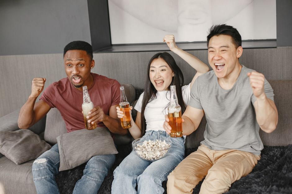 Grupo de amigos celebrando e se divertindo assistindo a um jogo ou evento esportivo em casa.