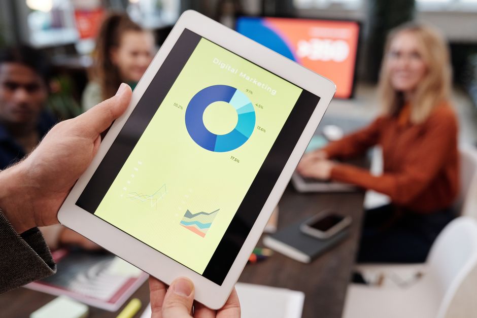 Pessoa apresentando dados de marketing digital em um tablet durante uma reunião de equipe.