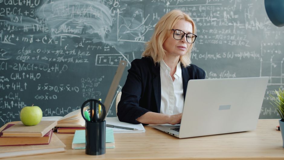 Professora de ciências ou matemática estudando em sala de aula com quadro cheio de equações ao fundo, em um ambiente de ensino ou pesquisa.