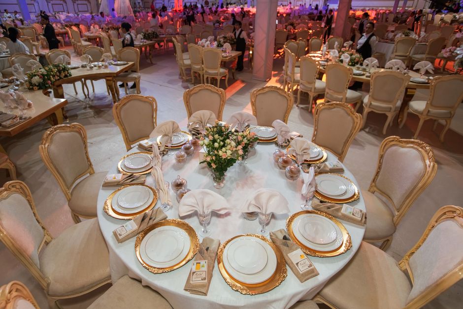 Mesa decorada para festa ou evento social com assembleia de pratos, talheres e centro de flores, pronta para receber convidados em um ambiente elegante.