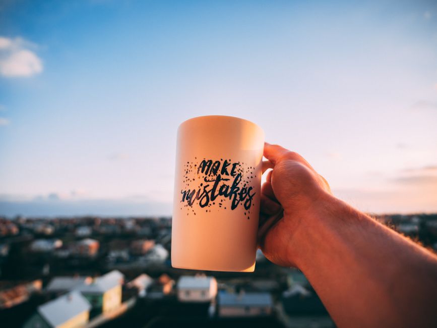 Mão segurando uma caneca com a frase 'Make Mistakes' ao pôr do sol, transmitindo a ideia de coragem para aprender com os erros, ideal para um artigo sobre crescimento pessoal ou inovação.