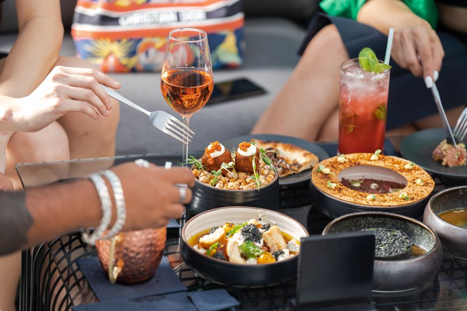 Reunião social com refeições sofisticadas, bebidas coloridas e atmosfera descontraída ao ar livre.