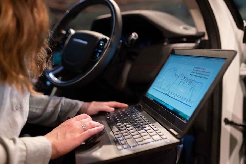 Pessoa analisando dados financeiros em um laptop dentro de um veículo, destacando a relação entre tecnologia e gestão financeira móvel.