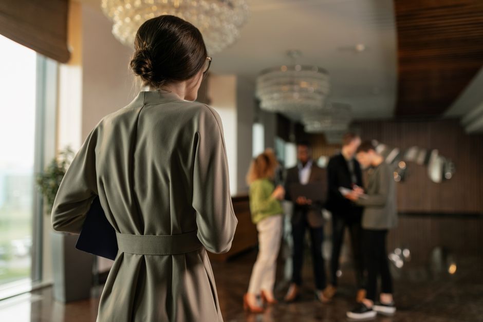 Mulher observando uma fila de pessoas em um ambiente corporativo ou de eventos profissionais, com foco na profissionalidade e networking.
