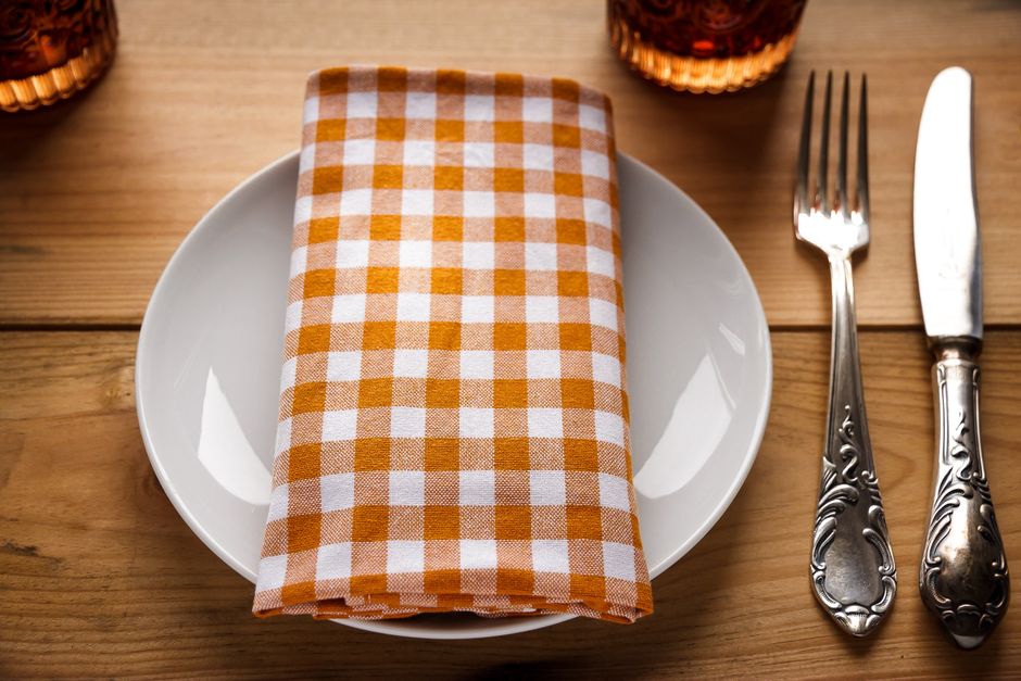 Configuração de mesa com prato, guardanapo xadrez e utensílios, demonstrando preparação para uma refeição em ambiente aconchegante.