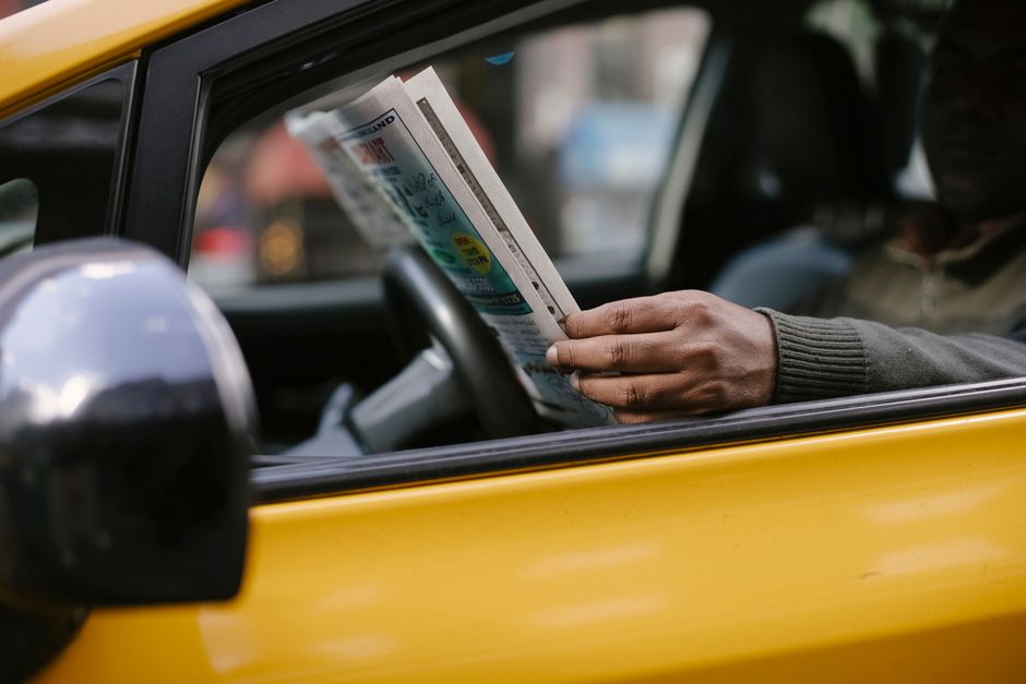 Pessoa lendo jornal dentro de um carro amarelo, representando segurança e rotina no transporte urbano.
