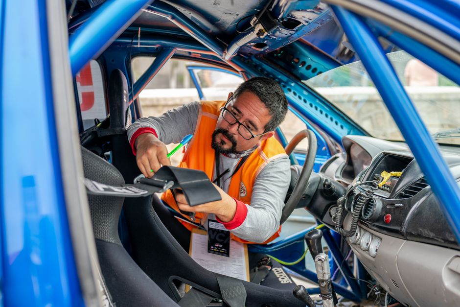 Homem realizando inspeção ou manutenção em um carro de corrida dentro de uma oficina especializada.
