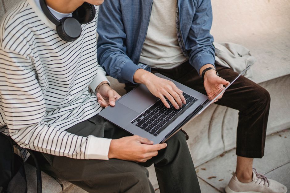 Homens colaborando em projeto de tecnologia usando laptop ao ar livre, destacando inovação e trabalho em equipe.