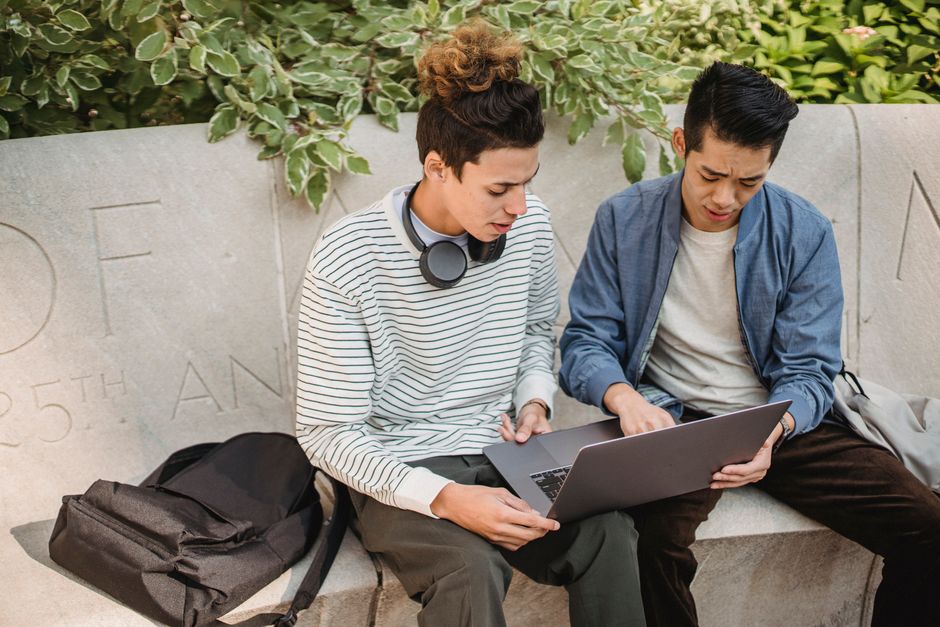 Jovens estudantes compartilhando conhecimento e colaborando ao usar um laptop ao ar livre, representando aprendizado e trabalho em equipe.