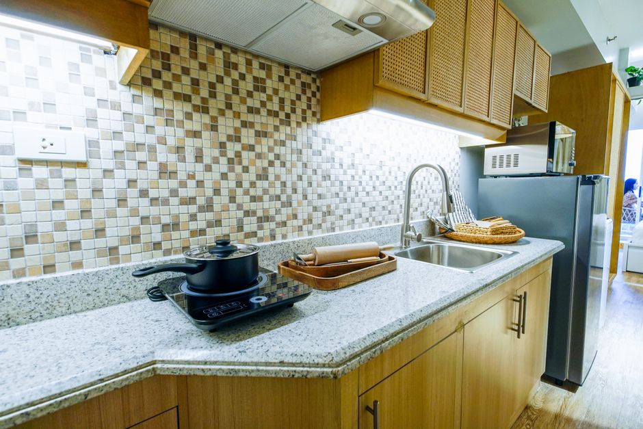 Cozinha moderna com bancada de granito, armários de madeira, revestimento de azulejos coloridos e eletrodomésticos, ideal para conteúdo sobre decoração e organização de ambientes residenciais.