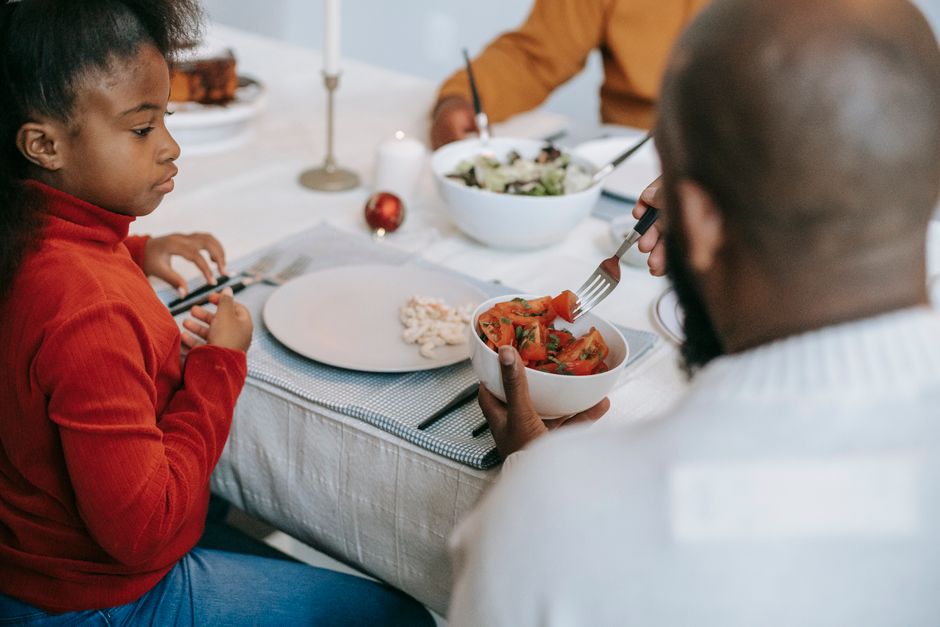Pessoa ajudando uma criança a comer salada em uma refeição familiar durante um almoço em família.