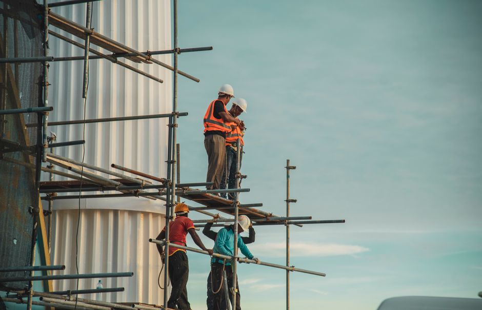 Homens utilizando equipamentos de segurança enquanto trabalham na construção de uma estrutura, destacando a importância da segurança e do trabalho em equipe na construção civil.
