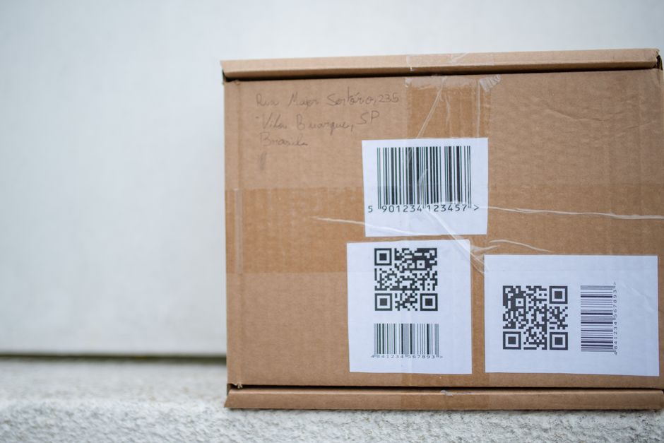 Imagem de uma caixa de papelão com etiquetas de código de barras e QR Code, relacionada ao tema de logística ou comércio eletrônico.