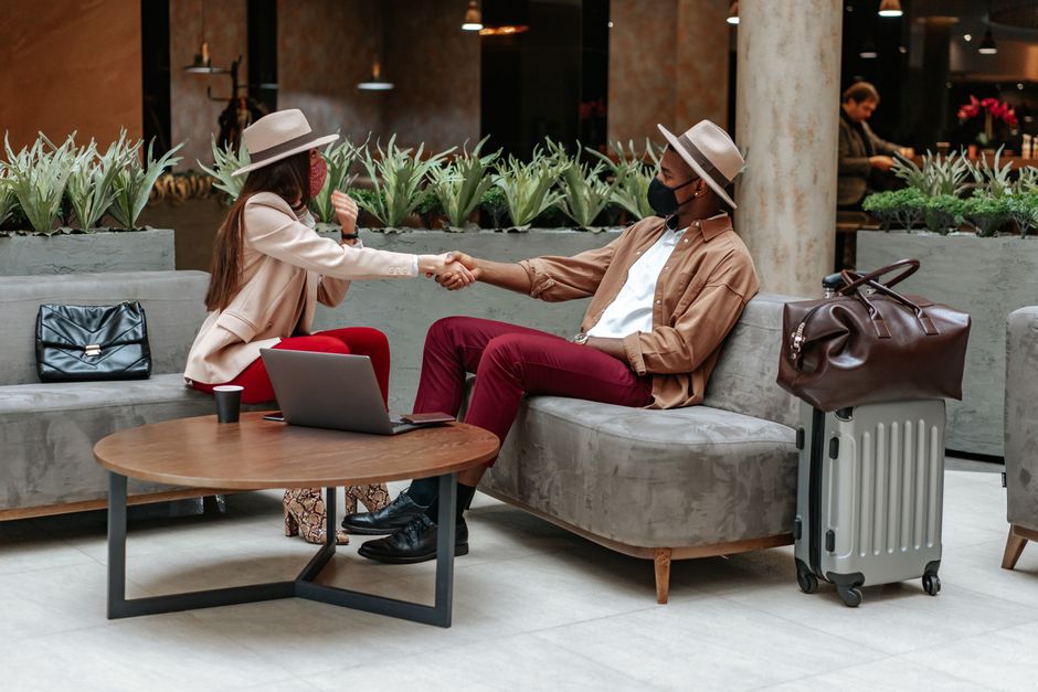 Dois viajantes se cumprimentando em um ambiente de espera, simbolizando boas-vindas ou início de uma interação profissional ou de viagem.