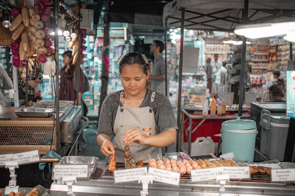 Vendedora preparando espetinhos em uma feira ao ar livre, exibindo cultura alimentar local.