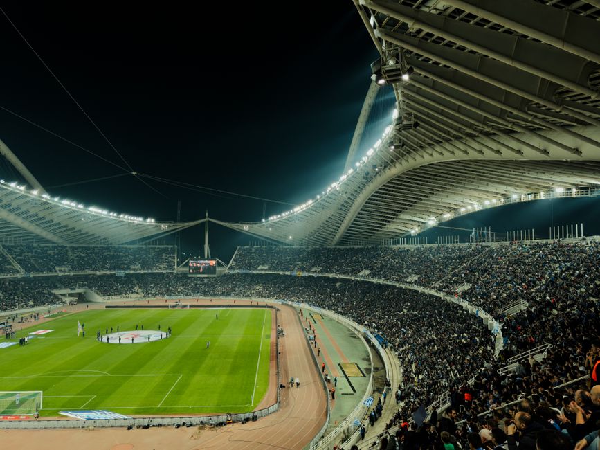 Estádio de futebol lotado durante uma partida noturna, com torcedores assistindo ao jogo.