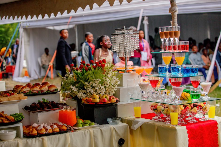 Mesa de festa ao ar livre com sobremesas, frutas e bebidas coloridas, em evento social sob uma tenda.