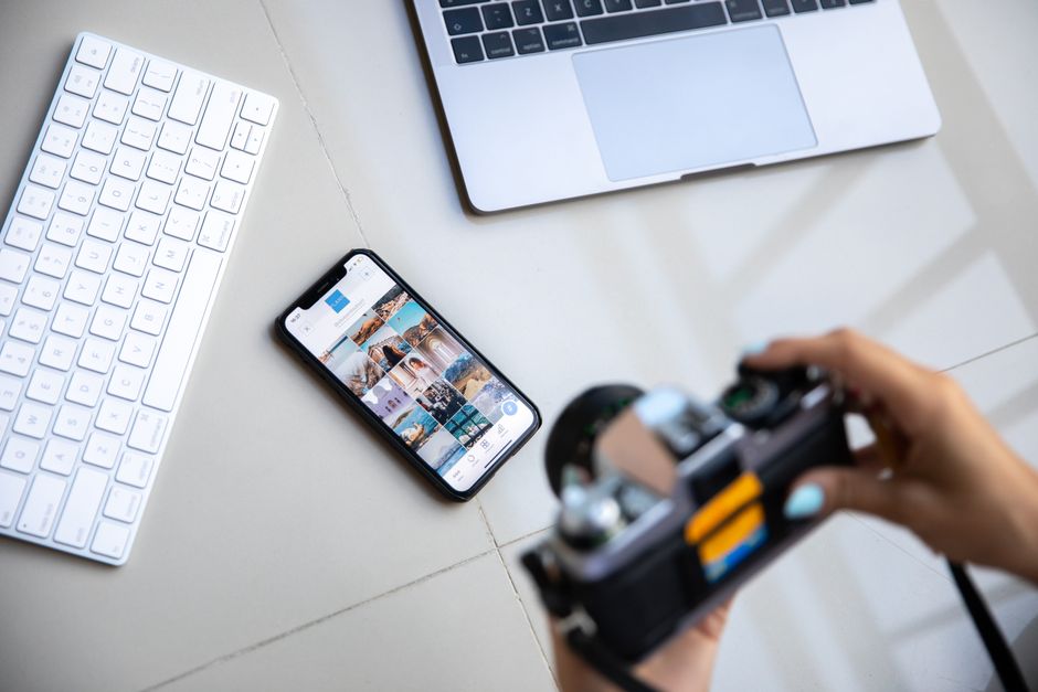 Imagem de um ambiente de trabalho com computador, smartphone exibindo fotos, e uma pessoa segurando uma câmera, ideal para um blog sobre produção de conteúdo e fotografia digital.