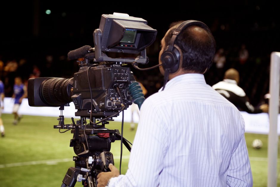 Profissional de televisão gravando uma transmissão ao vivo de um evento esportivo, com câmeras de alta tecnologia e equipe de produção.