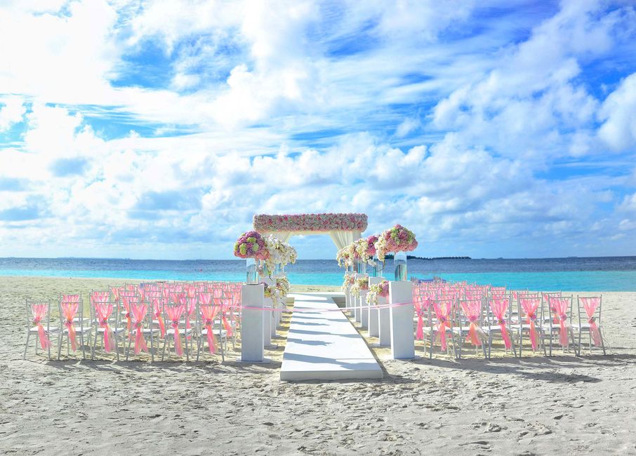 Estrutura decorativa de casamento na praia, com cadeiras e altar floral sob céu ensolarado.