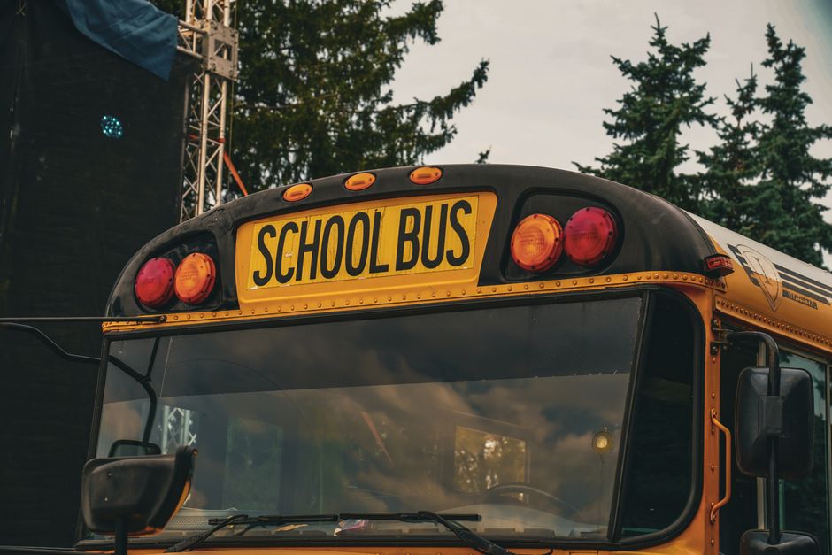 Imagem de um ônibus escolar amarelo, destacando o tema transporte escolar para crianças e adolescentes, com árvores ao fundo e céu nublado.