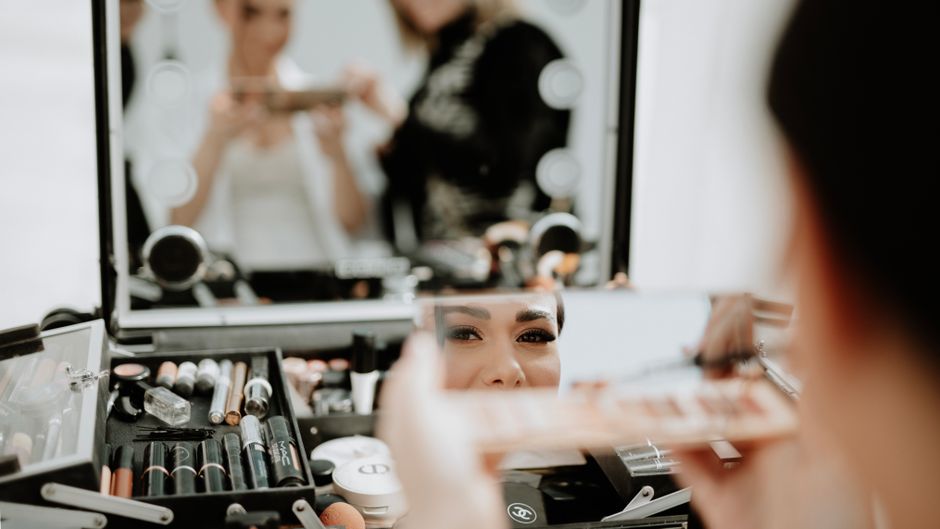 Mulher se maquiando em frente ao espelho, destaque para produtos de beleza e a preparação para algum evento ou rotina de cuidados pessoais.