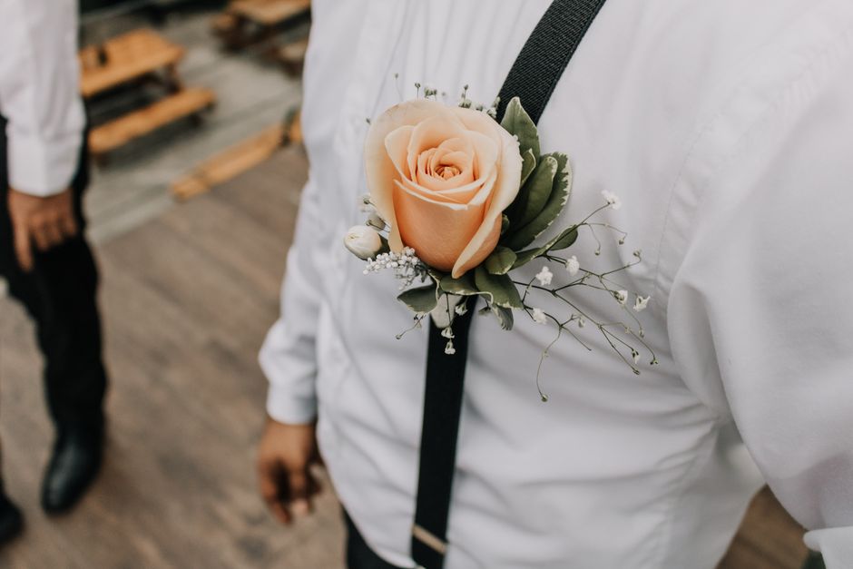 Homem vestido de branco com flor na lapela, simbolizando celebração ou ocasião especial.