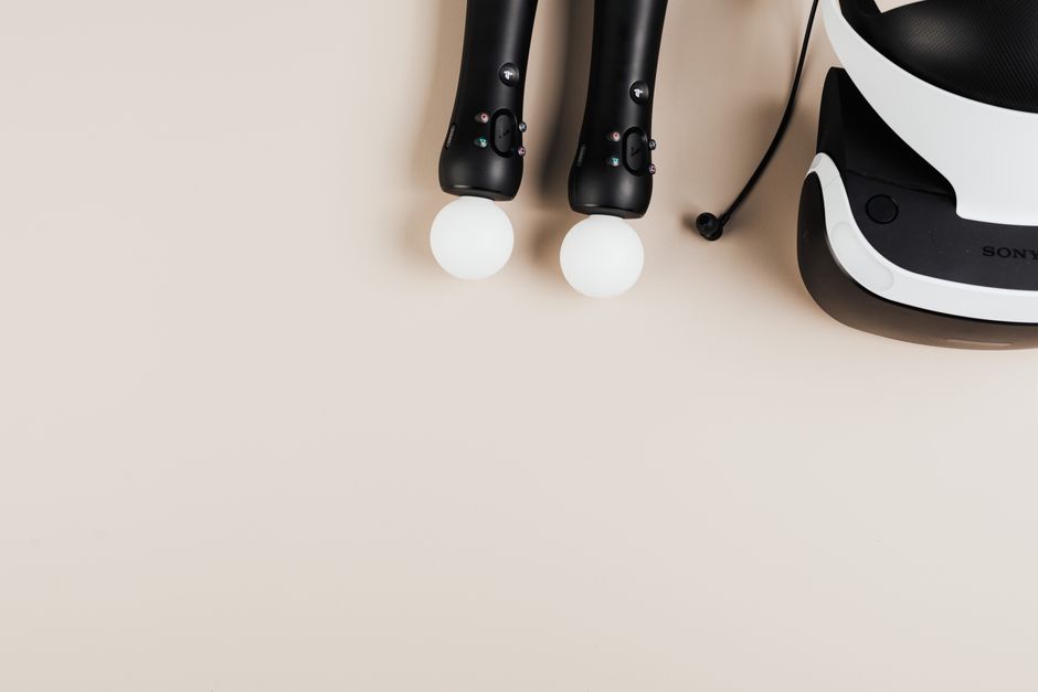 Imagem de controles de videogame com luzes acessas e um headset de realidade virtual sobre uma superfície clara, ideal para artigos sobre tecnologia e entretenimento digital.