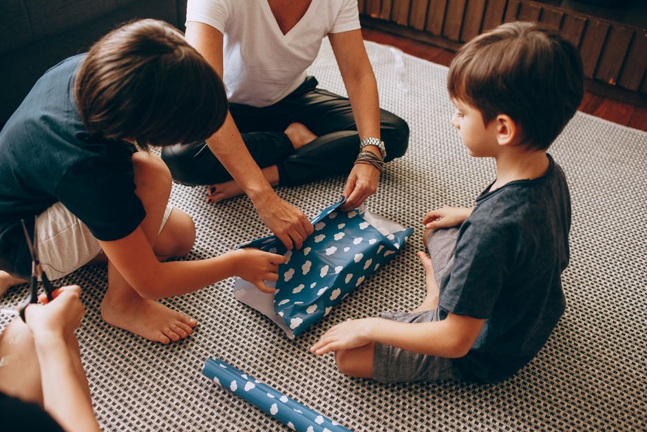 Crianças e um adulto envoltos na troca de presentes em um momento de celebração familiar, destacando o espírito de Natal ou aniversário.