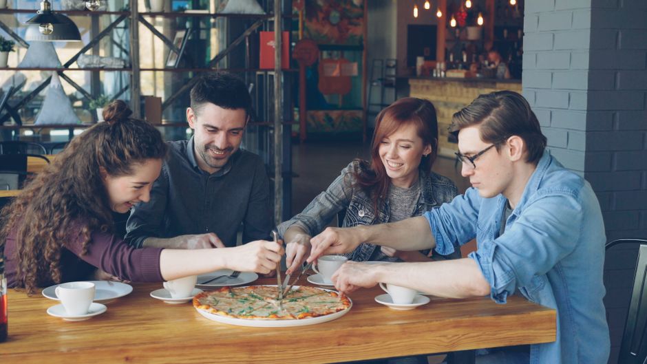 Grupo de amigos celebrando e compartilhando uma pizza em um restaurante acolhedor, demonstrando momentos de convivência e alegria.