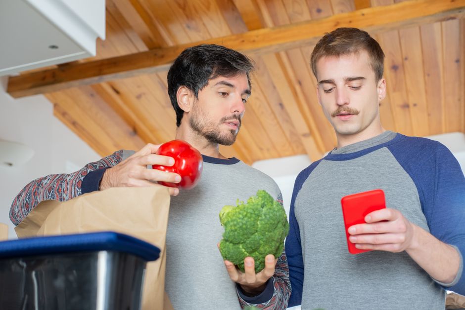 Dois jovens discutem sobre alimentação saudável enquanto estão na cozinha, analisando uma lista de compras.