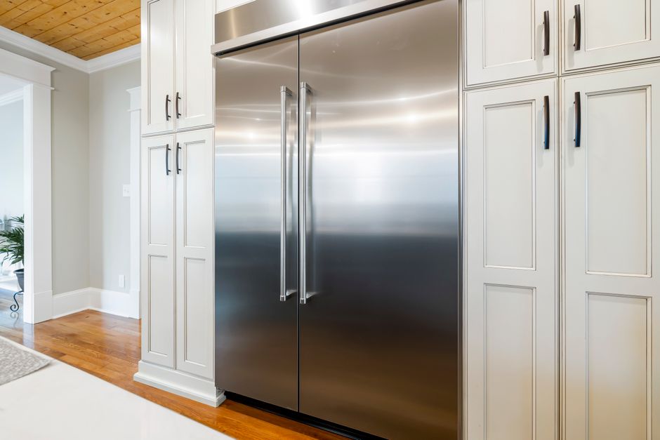 Imagem de uma cozinha moderna com geladeira de aço inox embutida entre armários brancos, destacando a organização e a elegância do ambiente.