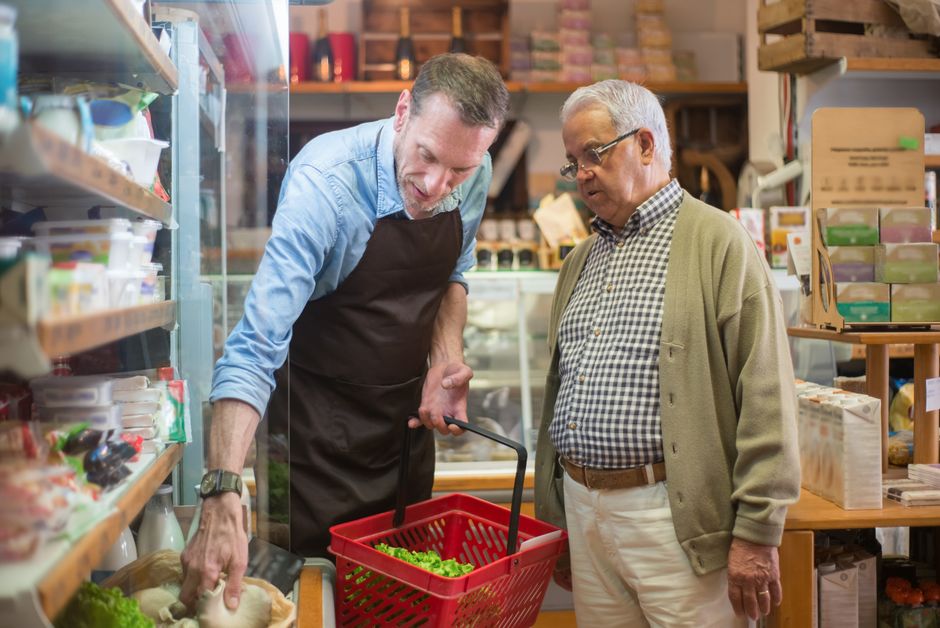 Dois homens conversando em uma loja de alimentos naturai, uma pessoa segurando uma cessa de alface dentro de uma cesta de compras.