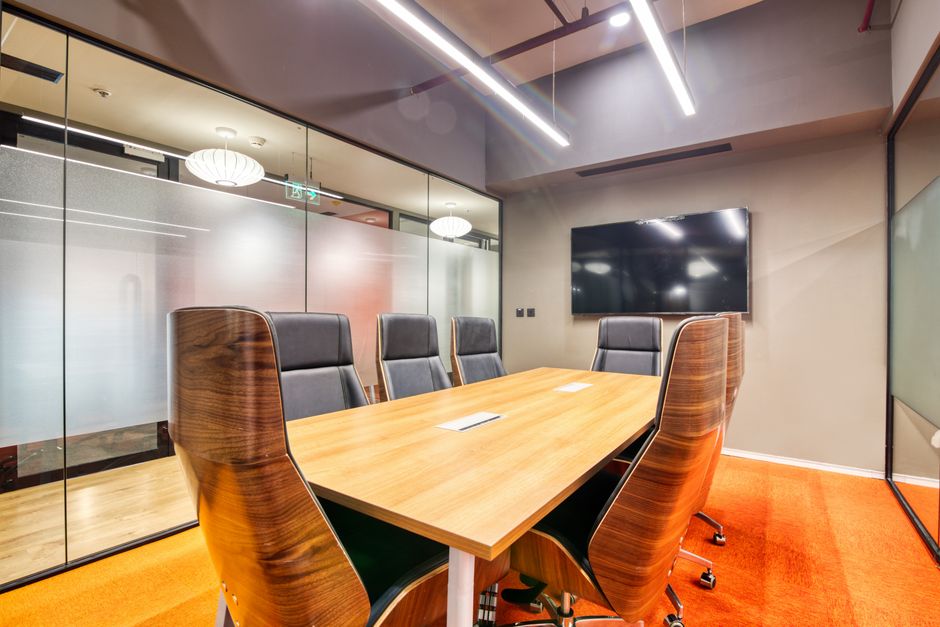 Sala de reunião moderna com mesa de madeira, cadeiras confortáveis e tela de televisão, ideal para apresentações e discussões empresariais.