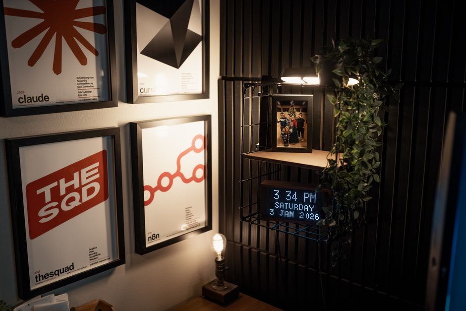 Imagem de um espaço de trabalho com decoração moderna, incluindo quadros na parede, uma luminária estilosa e uma planta, criando um ambiente aconchegante e artístico.