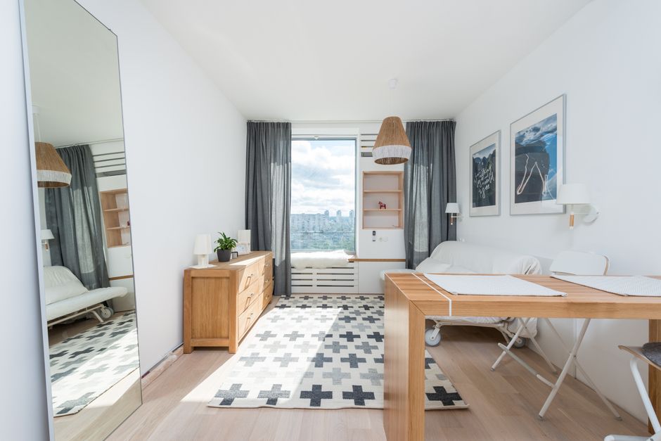 Imagem de um ambiente de apartamento bem iluminado, com decoração moderna e janelas grandes com vista urbana, ideal para artigos sobre decoração de interiores ou moradia urbana.