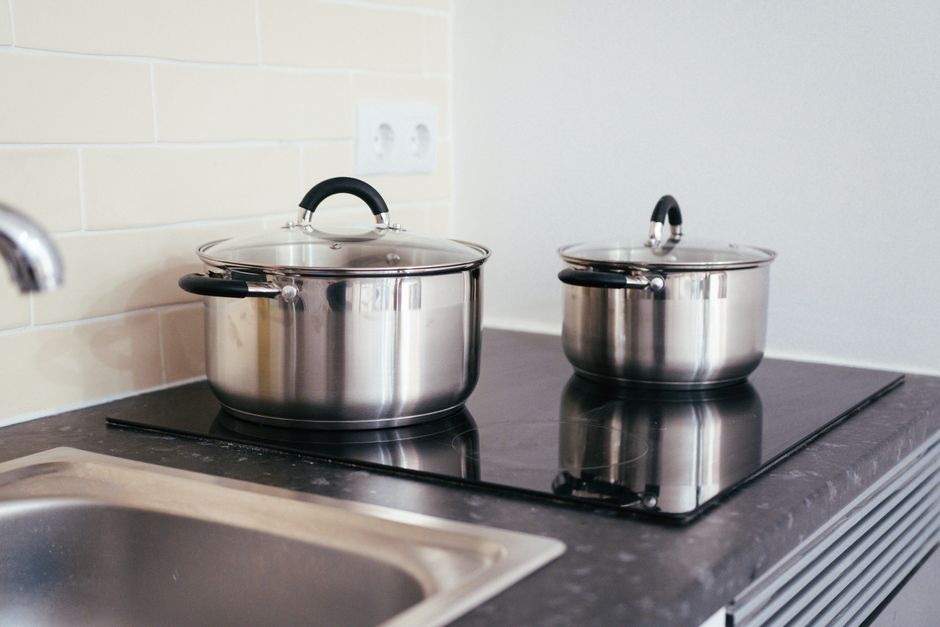 Imagem de duas panelas de inox sobre um fogão elétrico em uma cozinha moderna, demonstrando ambiente doméstico ou culinária.