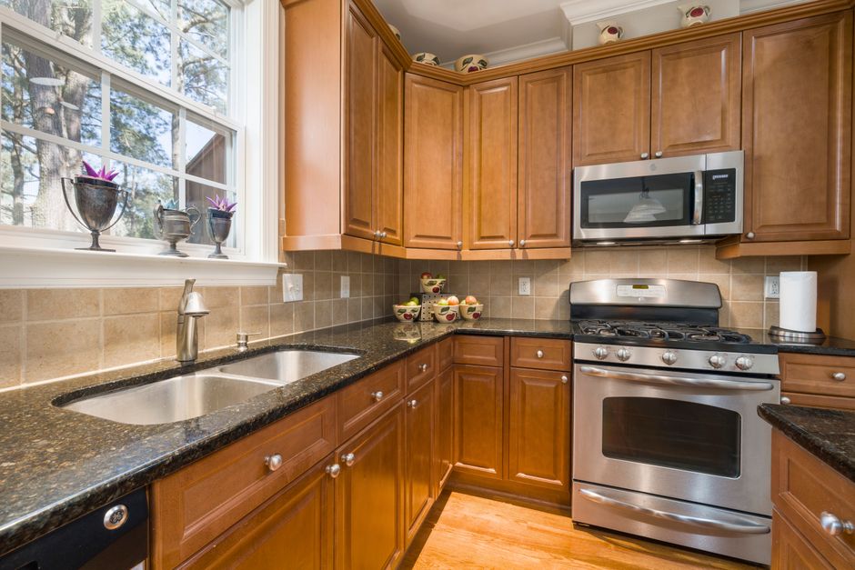 Cozinha moderna com armários de madeira, bancada de granito, eletrodomésticos em aço inox e janela com vista para uma área externa, transmitindo aconchego e funcionalidade.