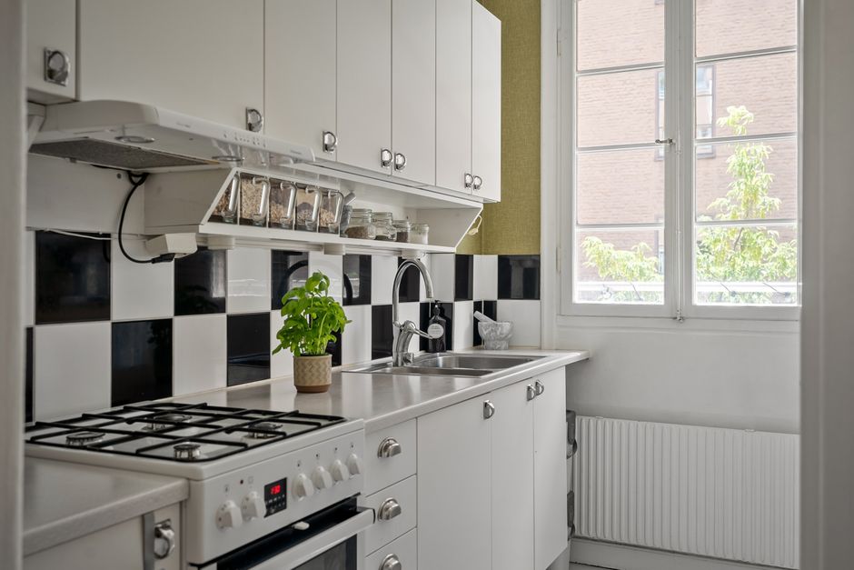 Cozinha moderna com armários brancos, detalhes em preto e branco na parede, janelas amplas trazendo iluminação natural, trazendo uma atmosfera aconchegante e funcional para o ambiente doméstico.