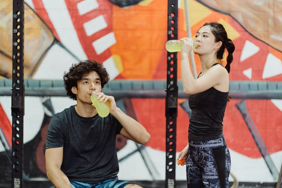 Jovens praticando exercícios físicos após o treino, simbolizando saúde e bem-estar num ambiente de academia com grafite ao fundo.