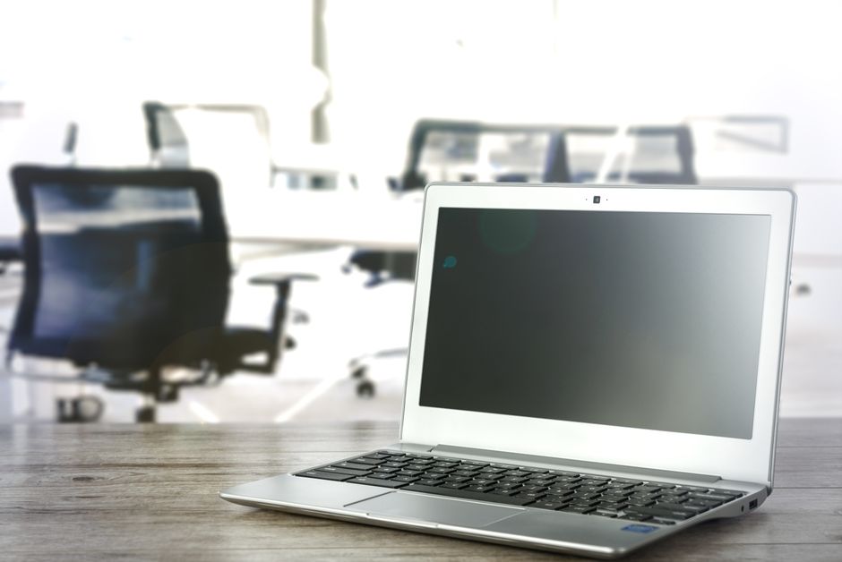 Imagem de uma sala de reunião moderna com uma mesa e cadeiras, destacando um laptop aberto ao centro, simbolizando trabalho colaborativo e reuniões de negócios.