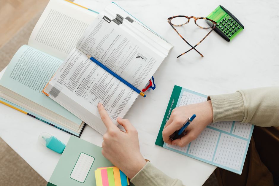 Pessoa estudando e analisando documentos e relatórios em um ambiente de trabalho acadêmico ou profissional.