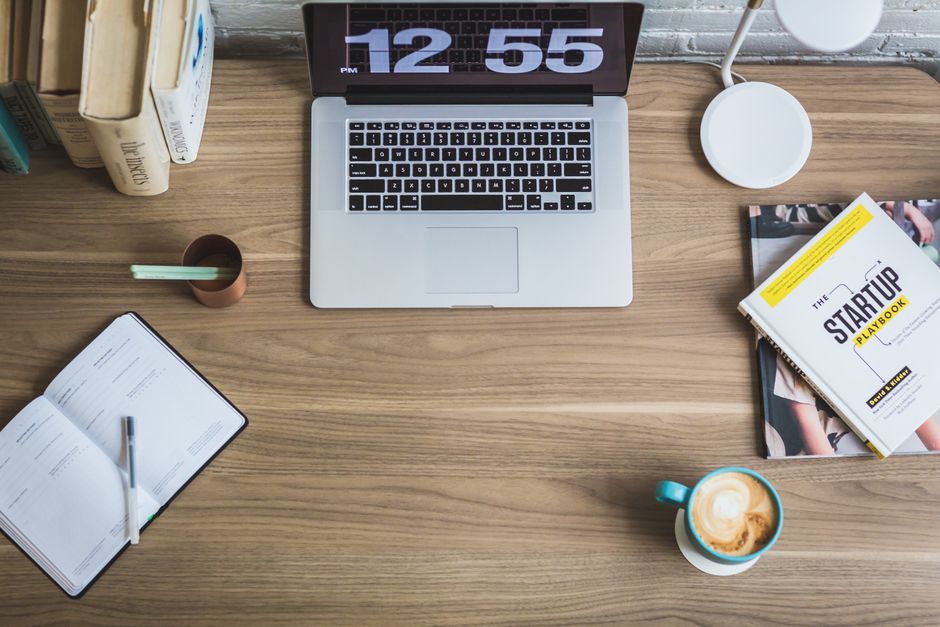 Mesa de trabalho com foco em empreendedorismo e planejamento de startups, contendo livros, celular, café e materiais de leitura profissional.