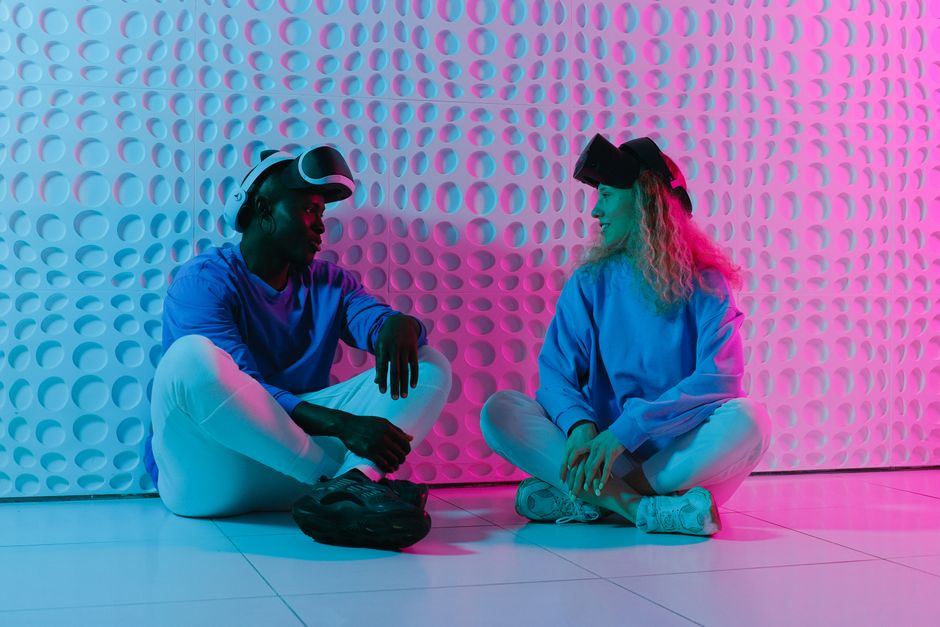 Dois jovens usando óculos de realidade virtual em um ambiente com iluminação de LED rosa e azul, representando tecnologia e inovação digital.