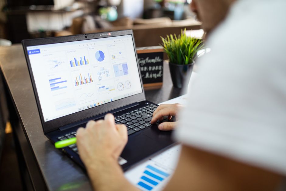 Pessoa analisando gráficos e dados financeiros em um laptop, evidenciando o tema de gestão e análise de informações empresariais.