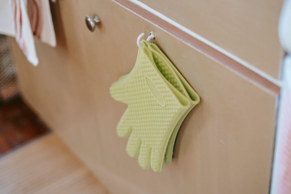 Luvas de limpeza penduradas em cabide na cozinha, representam organização e rotina doméstica.