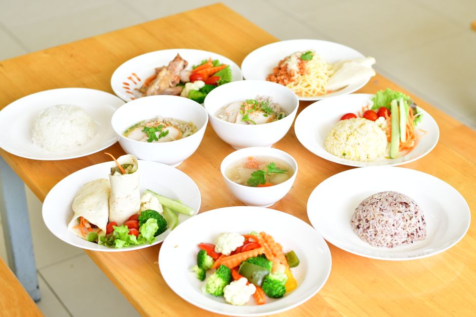 Variedade de pratos tradicionais de uma refeição equilibrada, incluindo arroz, verduras, carnes e sopas, dispostos em pratos brancos sobre uma mesa de madeira.
