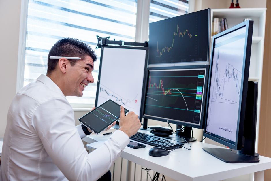 Homem analisando dados financeiros em múltiplas telas de computador, em um ambiente de trabalho de alta tecnologia.